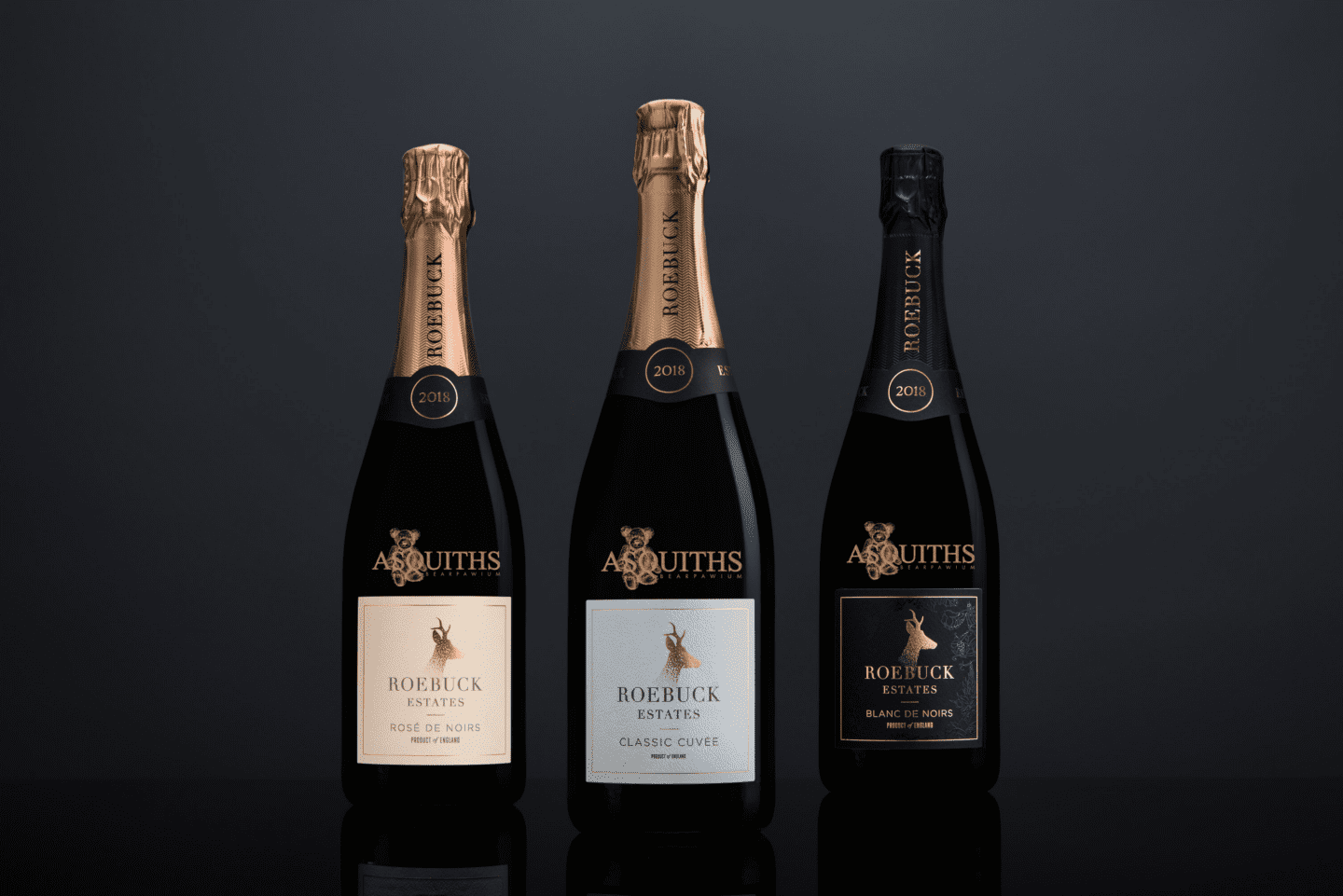 Three engraved bottles of Roebuck Estates sparkling wine, including Rosé de Noirs, Classic Cuvée, and Blanc de Noirs, against a dark background.”